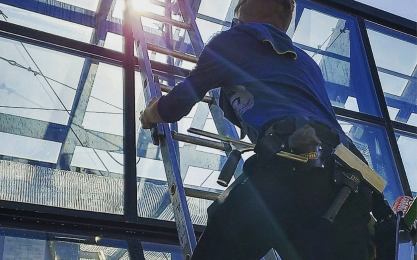 Dylan cleaning commercial glass from a ladder with sun flare