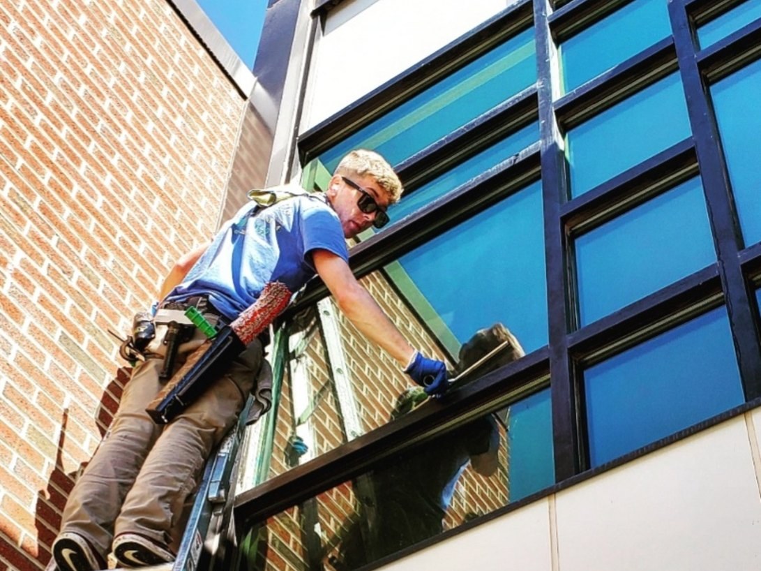 Dylan cleaning tall exterior windows with ladder and professional tools